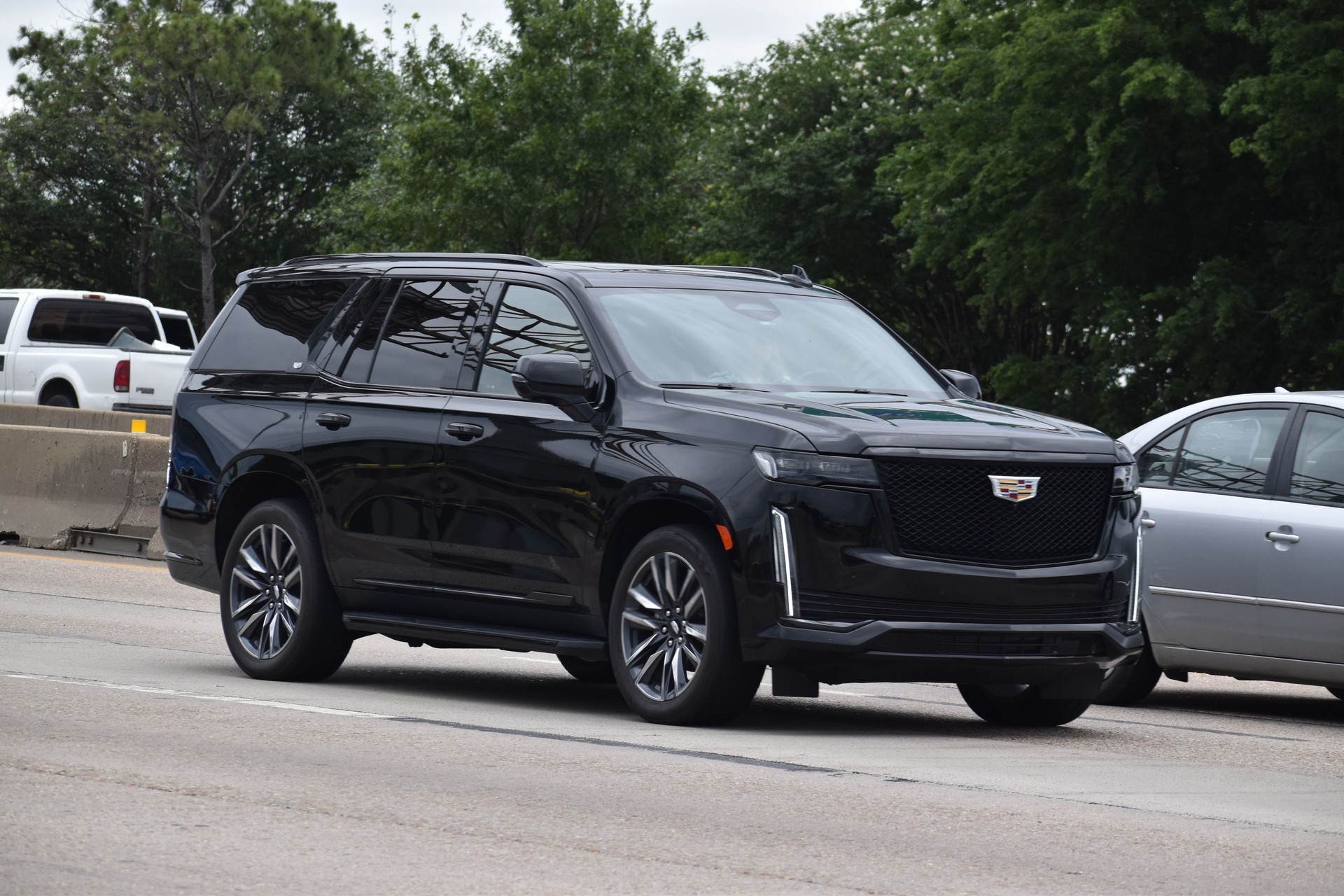 A portrait of a luxury black Cadilac Escalade ESV traveling down a highway in moderate traffic